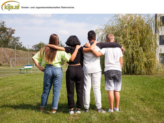 4 Kinder stehen mit dem Rücken zur Kamera und umarmen sich.