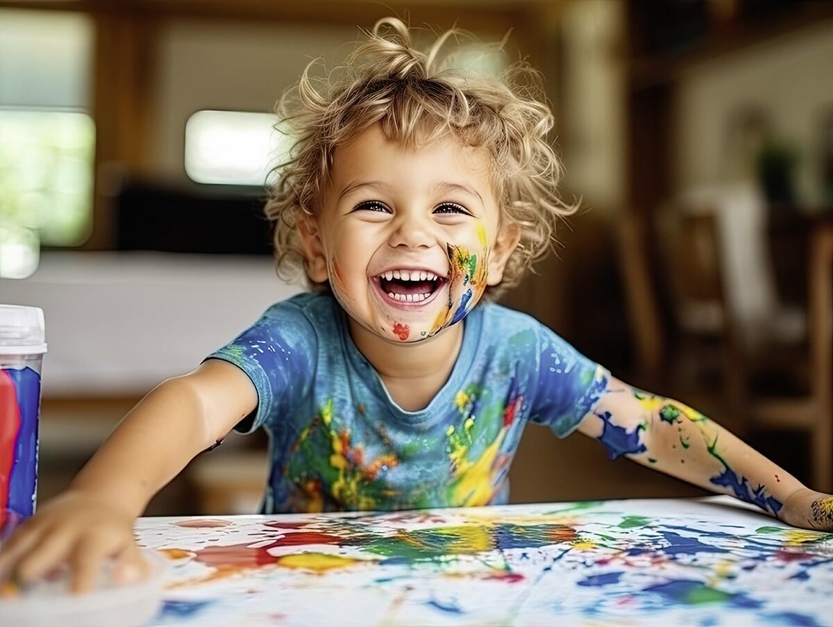 Ein fröhlich lachendes Kleinkind ist mit Fingerfarben bunt bekleckert.