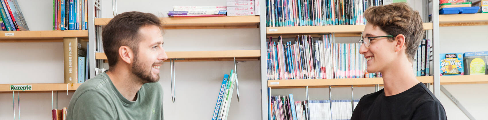 Ein Mann und ein Junge im Gespräch vor einer Bücherwand