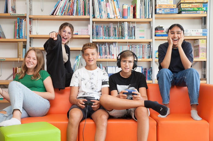 Eine Gruppe von Kindern sitzt auf der Couch uns spielt Computerspiele. 