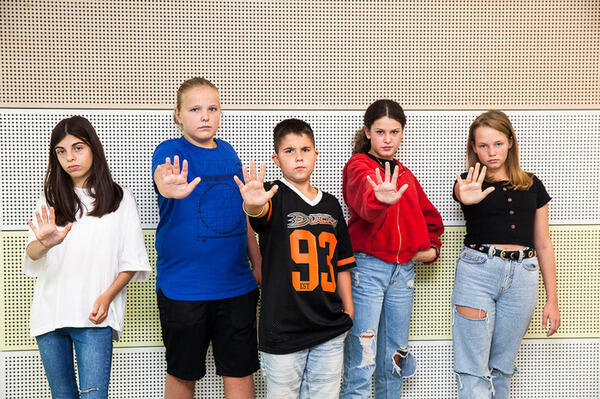 Eine Gruppe von Kindern steht vor einer Wand und macht eine Stopp Geste.